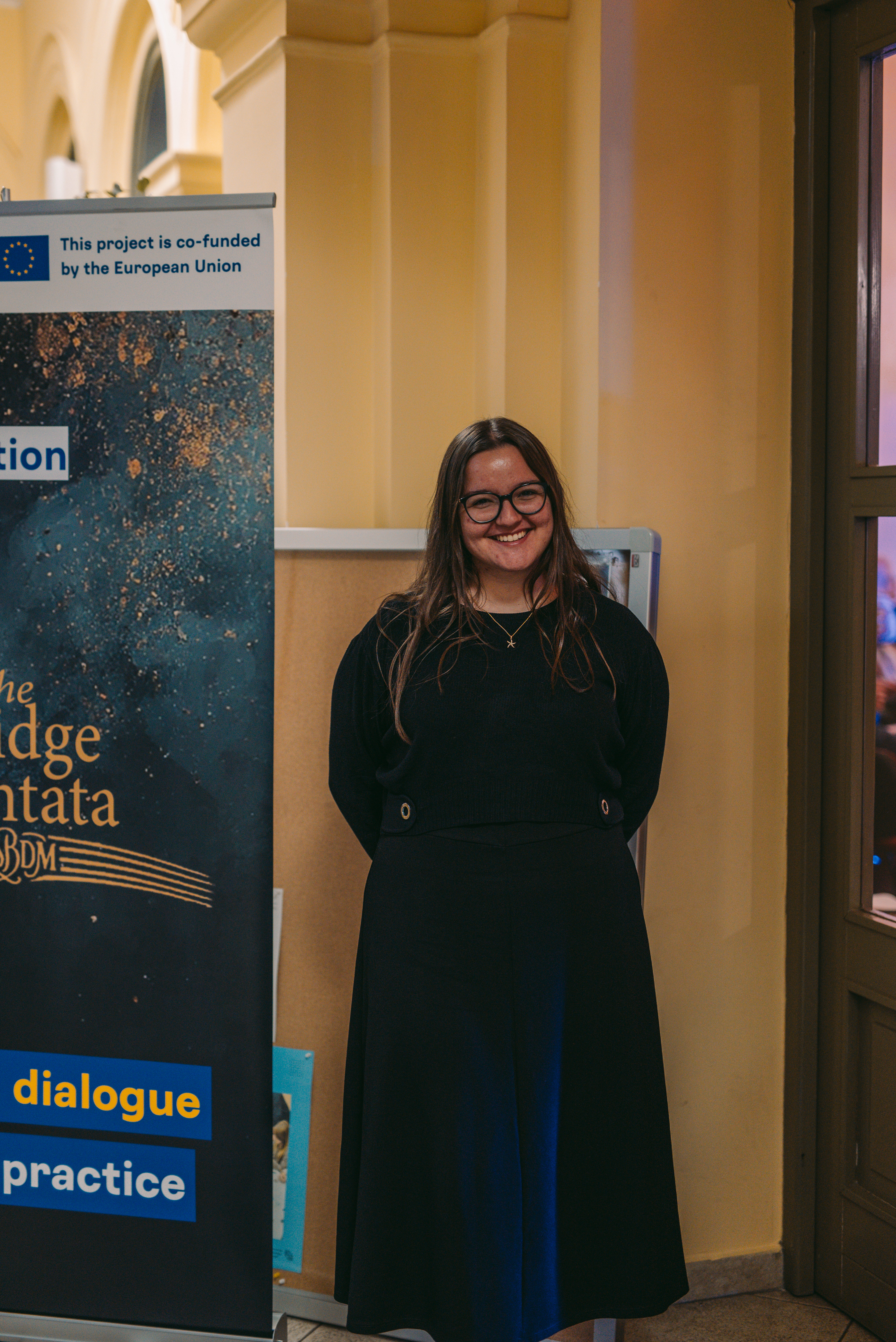 Portrait of a participant beside The Bridge Cantata event banner